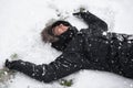 Young man laughing, with happy expression, snow covered, lying on the ground in snowfall. Royalty Free Stock Photo