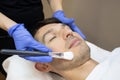 Young man laying on a facial therapy couch covered with the white towel with closed eyes. Facial therapist hands holding