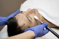 Young man laying on a facial therapy couch covered with the white towel with closed eyes. Facial therapist hands holding