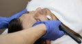 Young man laying on a facial therapy couch covered with the white towel with opened eyes. Facial therapist hands holding