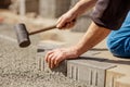 Young man laying gray concrete paving slabs in house courtyard on gravel foundation base. Master lays paving stones