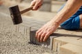 Young man laying gray concrete paving slabs in house courtyard on gravel foundation base. Master lays paving stones