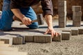 Young man laying gray concrete paving slabs in house courtyard on gravel foundation base. Master lays paving stones