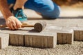 Young man laying gray concrete paving slabs in house courtyard on gravel foundation base. Master lays paving stones