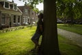 Young man leaning on his back in a tree, resting. Park in residential area with typical dutch houses.