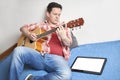 Young man learning to play guitar at home using his tablet Royalty Free Stock Photo