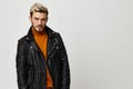 young man in leather jacket blond orange sweater light background