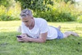 Young man lies on the grass, looks into a smartphone, listens to music with wireless headphone Royalty Free Stock Photo