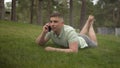 A young man lies on the grass and talks on the phone. A student in the park rests on the grass with communicates by Royalty Free Stock Photo