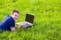 Young man lies on green grass with laptop and working Royalty Free Stock Photo