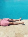 A young man lies on poolside at resort hotel during vacation. Close up of male legs near turquoise water Royalty Free Stock Photo