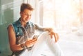 Young man listen music with headphones and smartphone sitting on windowsill