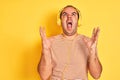 Young man listening to music using headphones standing over isolated yellow background crazy and mad shouting and yelling with Royalty Free Stock Photo