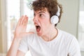 Young man listening to music wearing headphones at homes shouting and screaming loud to side with hand on mouth Royalty Free Stock Photo