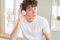 Young man listening to music wearing headphones at homes smiling with hand over ear listening an hearing to rumor or gossip Royalty Free Stock Photo