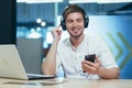 A young man listens to podcasts in headphones, holds a mobile phone in his hands, talks on video communication. Sitting at work in Royalty Free Stock Photo