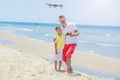 Young man with little boy flying drone at the sea shore, enjoying summer vacation.