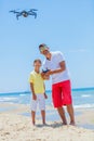 Young man with little boy flying drone at the sea shore, enjoying summer vacation.