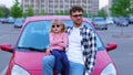Young man and little girl in eyeglasses posing near red car outdoors. Guy showing thumb up. Family, transport, trip Royalty Free Stock Photo