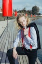 Young man with long blond hair in a suit in a red tie and suspenders calmly posing, throwing a black jacket over one shoulder Royalty Free Stock Photo