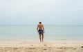 Young man with a long hair on a white sand beach and walks into tropical sea. Vacation and travel concept.