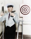 Young man looking at a mirror and aiming at a dartboard with a handgun