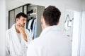 Young man looking in mirror in bedroom in the morning, daily routine. Royalty Free Stock Photo