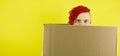 Young man looking out of cardboard box on yellow background in studio. Male courier hiding behind package. Concept of Royalty Free Stock Photo