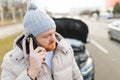 A young man looks angry and frustrated near his broken car and speaks on his mobile phone, Royalty Free Stock Photo