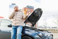 A young man looks angry and frustrated near his broken car and speaks on his mobile phone, Royalty Free Stock Photo