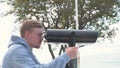 Young man looks through binoculars on observation deck. Media. Man looks through binoculars in rain in summer. Man is Royalty Free Stock Photo