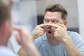 Young man looks in mirror and presses pimples on his nose