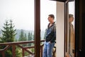 A young man looks out from the hotel`s balcony with a view of the mountains, the fog and the fir forest. Royalty Free Stock Photo