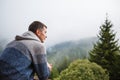 A young man looks out from the hotel`s balcony with a view of the mountains, the fog and the fir forest. Royalty Free Stock Photo