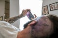 Young man looks at a picture on his cell phone of the tattoo he`s getting on his head.