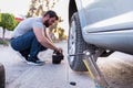 young man loosening a nut of his car tire, changing a flat tire on the road, car jack being used Royalty Free Stock Photo