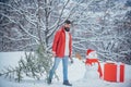 Young man lumberjack is cutting Christmas tree in the wood. Happy father with Christmas tree on a snowy winter walk. A Royalty Free Stock Photo