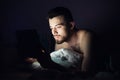 Young man lying on bed on his belly and look at tablet`s screen. Concentrated calm guy working playing games or Royalty Free Stock Photo