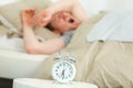 Young man lying in bed yawning near alarm clock Royalty Free Stock Photo