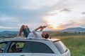 Young Man lying on the car roof and reading the paper bestseller book.He stopped his auto on the meadow with a beautiful valley Royalty Free Stock Photo