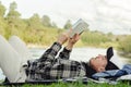 Young man lying on the grass by the river while reading book Royalty Free Stock Photo