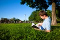 Young man lying on green grass in trees and reading book Royalty Free Stock Photo