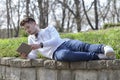 Young man lying in the park, holding a tablet in his hands and e Royalty Free Stock Photo