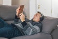 Young man lying and relaxing on the sofa while listening music and using a tablet. Guy having great time at home concept Royalty Free Stock Photo