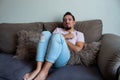 Young man in make-up with a pained gesture of sad concern sitting on the sofa in his house. LGBTIQ people culture and rights