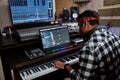 Young man, male artist looking focused while playing keyboard synthesizer, sitting in recording studio