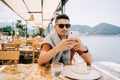 Young man male in sunglasses looking at his mobile smart phone gadget in a street sea side cafe restaurant coffee shop Royalty Free Stock Photo