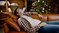 Young man in mask lies on sofa and stares at ceiling, suffering from loneliness and home isolation during Christmas holidays,