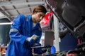 Young man is mechanic using laptop computer checking engine of car in the garage. Royalty Free Stock Photo