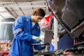 Young man is mechanic using laptop computer checking engine of car in the garage. Royalty Free Stock Photo